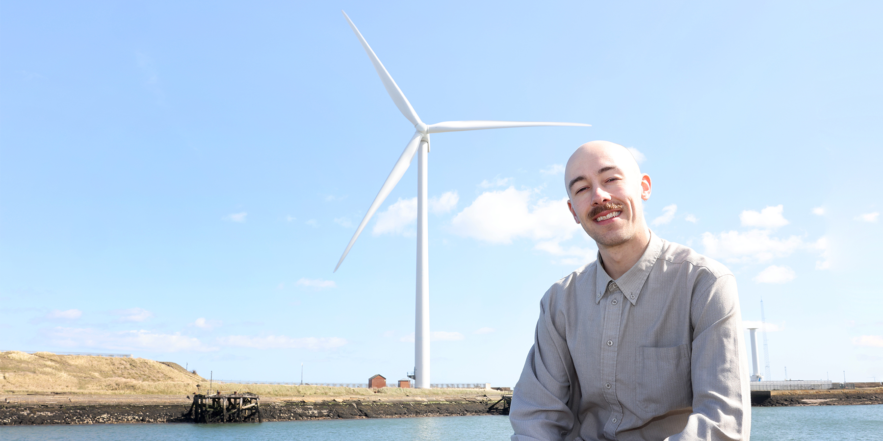 Image of Steven Ziolkowski sitting in front of a wind turbine on a sunny day.